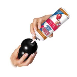 Hand using KONG toy filler to stuff a KONG Extreme rubber dog toy for extended playtime and enrichment.