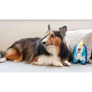 A dog lounging next to an Outward Hound Invincibles Mini Penguin squeaky toy on a sofa.